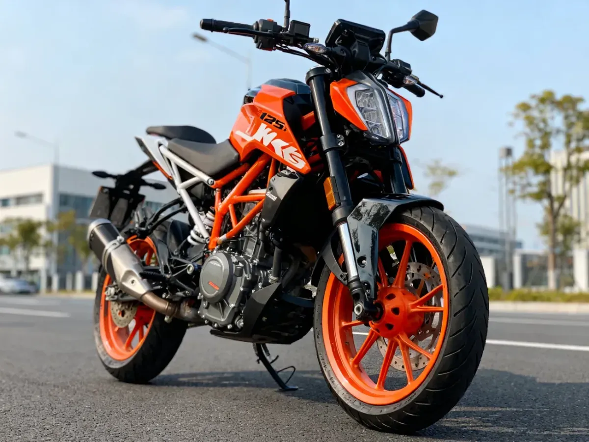 KTM Duke 125 z przodu na czystym asfalcie miasta, wyeksponowane felgi, hamulce i silnik w pomarańczowo-czarnej kolorystyce